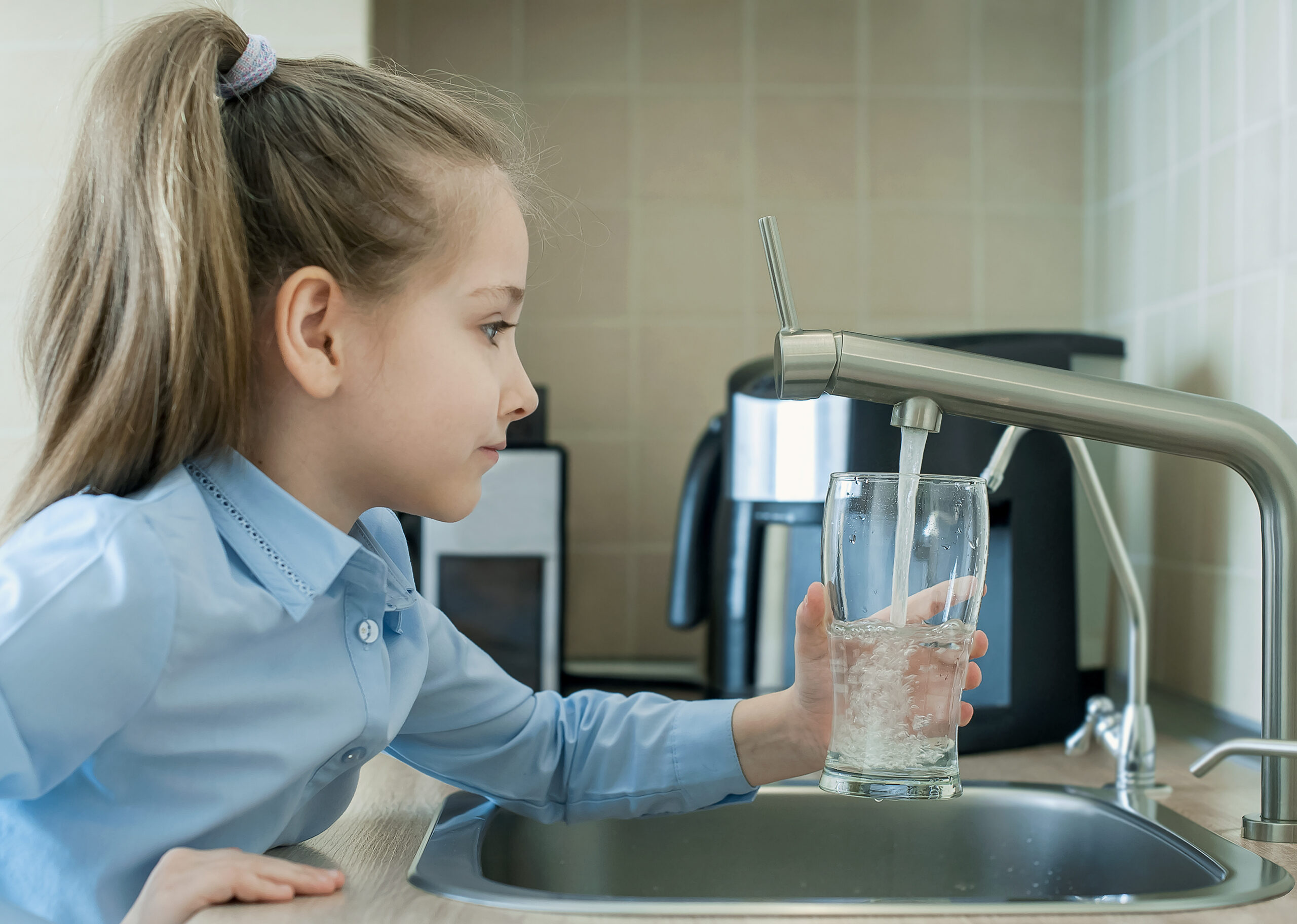 Child is holding a transparent glass. Filling cup beverage. Pouring fresh drink. Consumption of tap water contributes to the saving of water in plastic bottles and to the protection of the environment